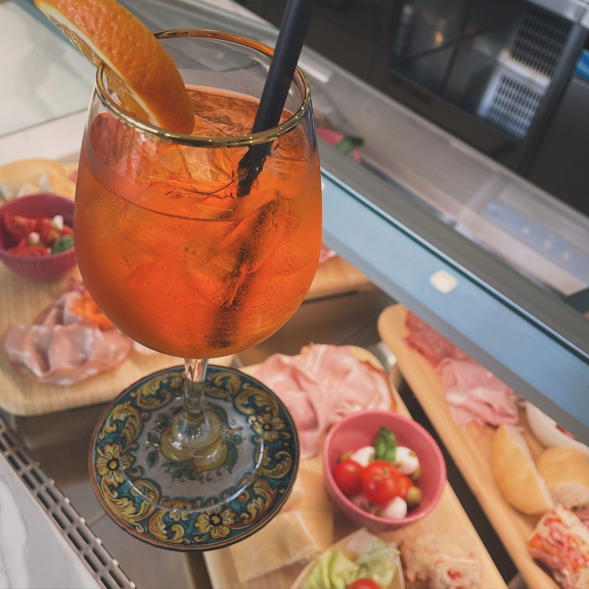 Cocktail Aperol Spritz con fetta d'arancia e cannuccia, accanto a un piatto di antipasti.
