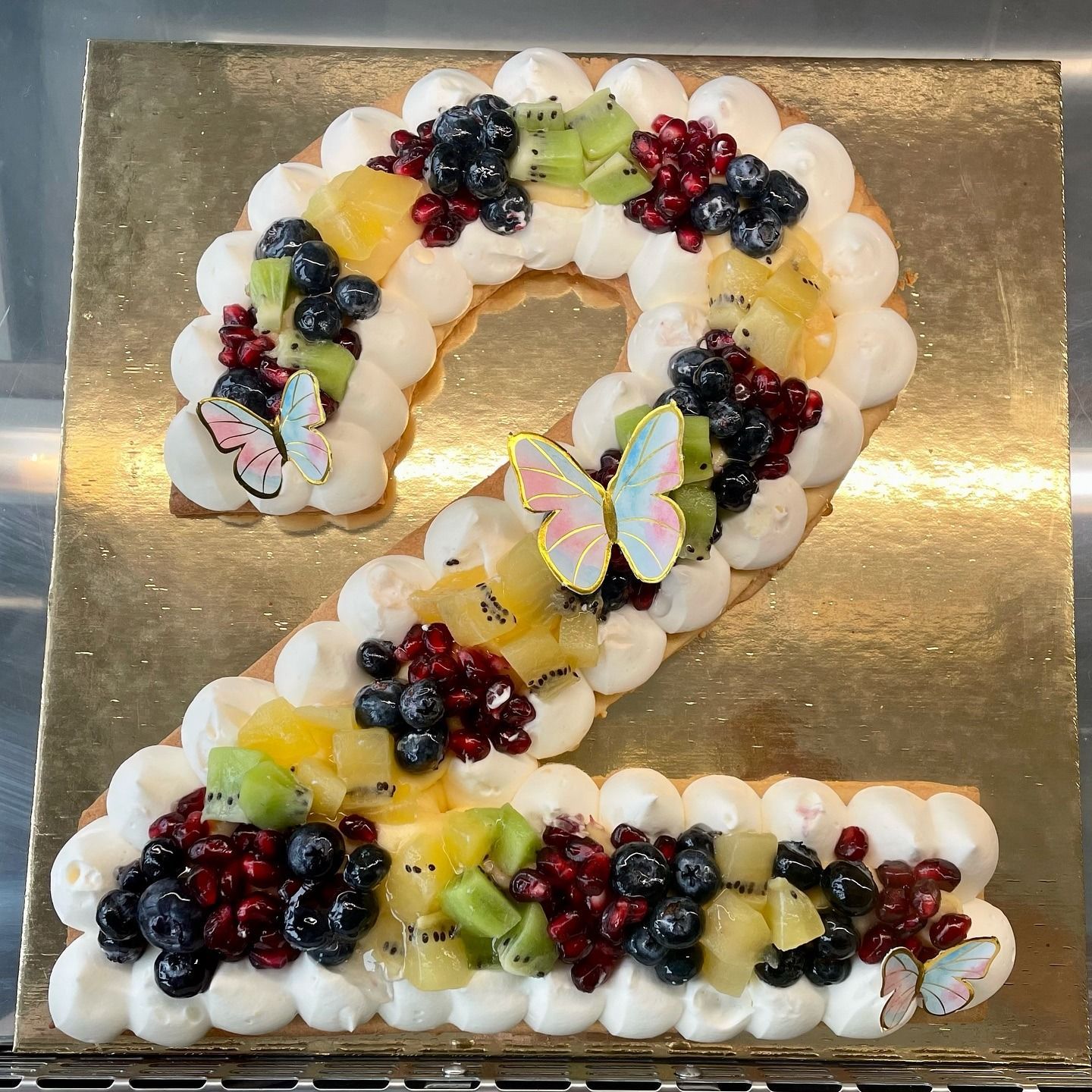 Una torta a forma di numero due, decorata con panna, frutta e decorazioni a farfalla.