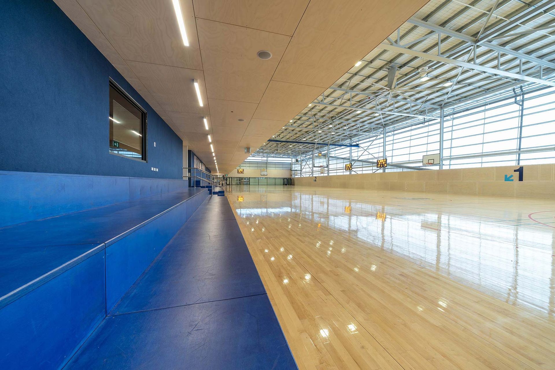 A large empty gym with a wooden floor and a blue bench.