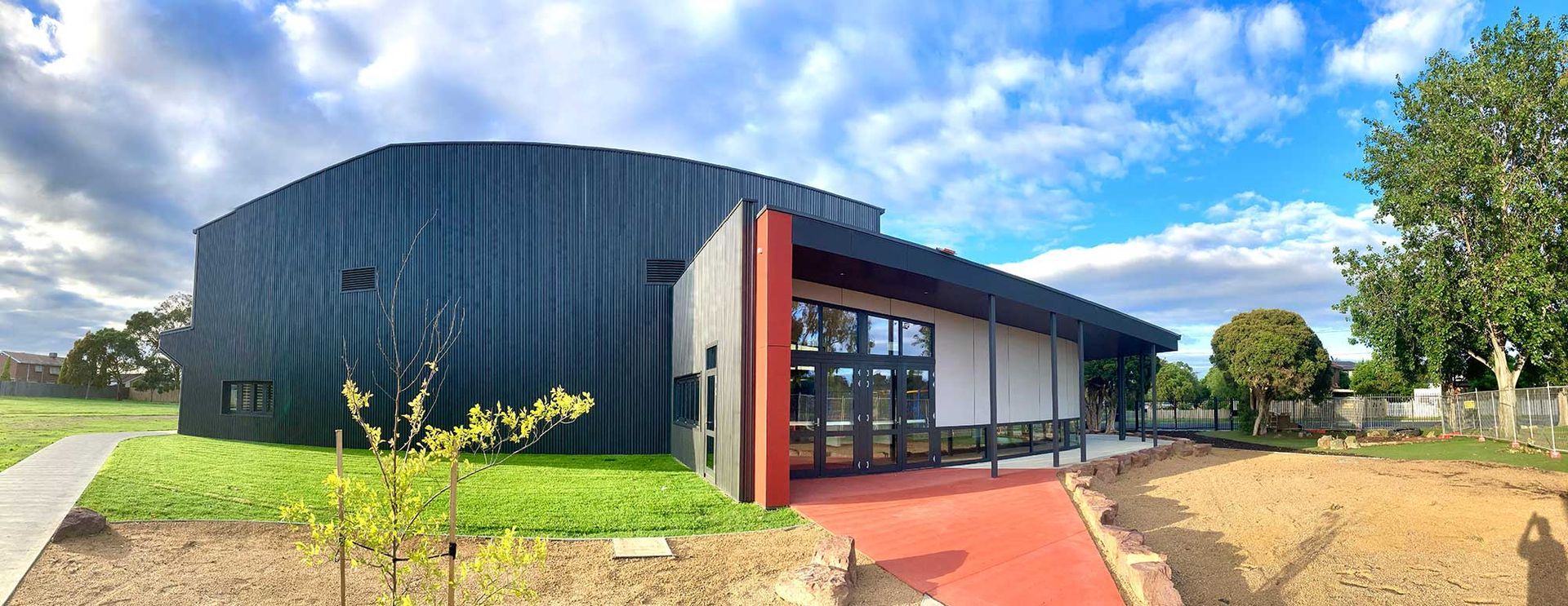 A large building with a red walkway leading to it is surrounded by grass and trees.
