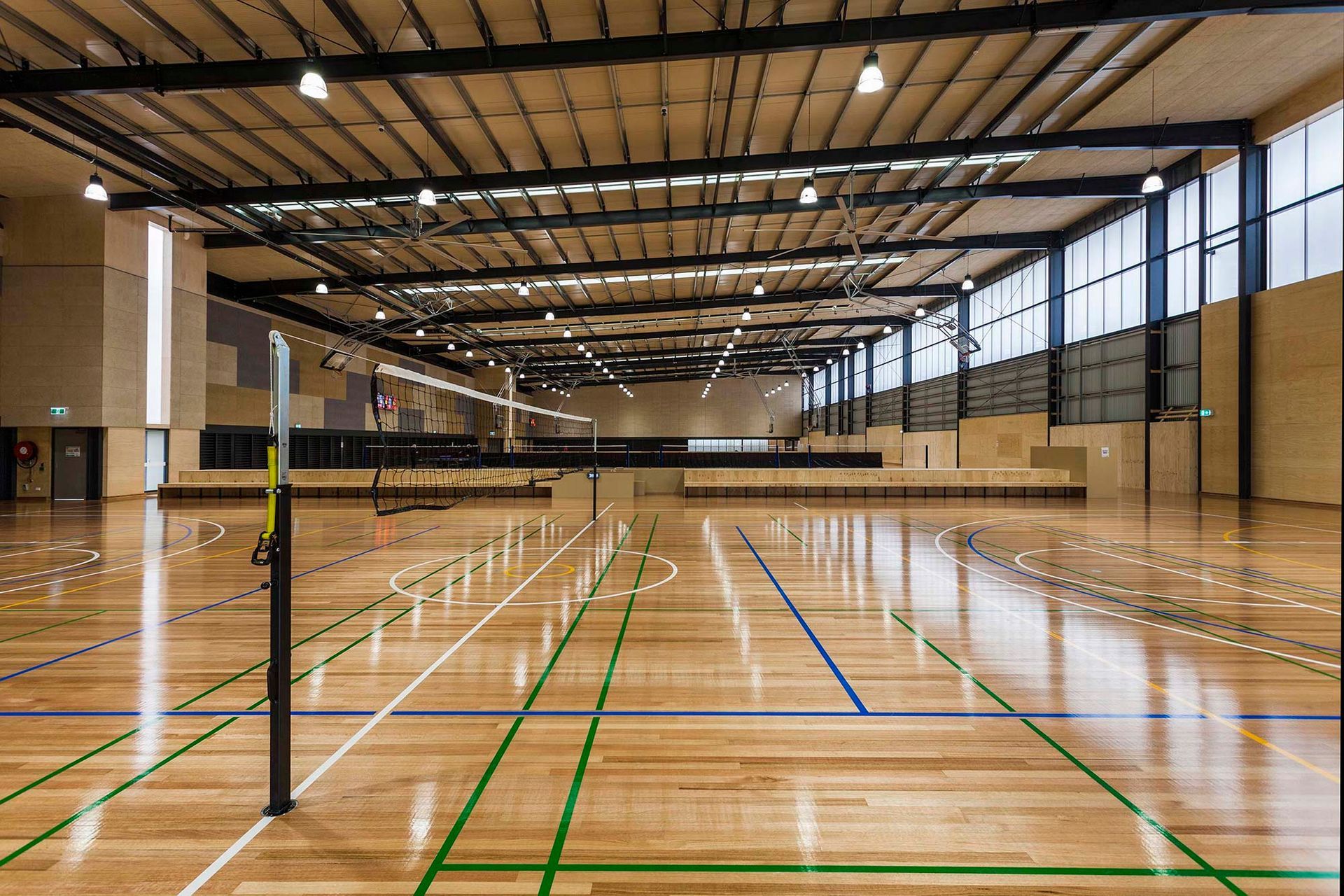 An empty gym with a wooden floor and a volleyball net