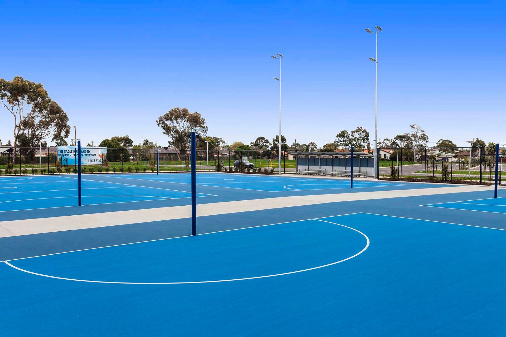 A blue basketball court with a fence and trees in the background
