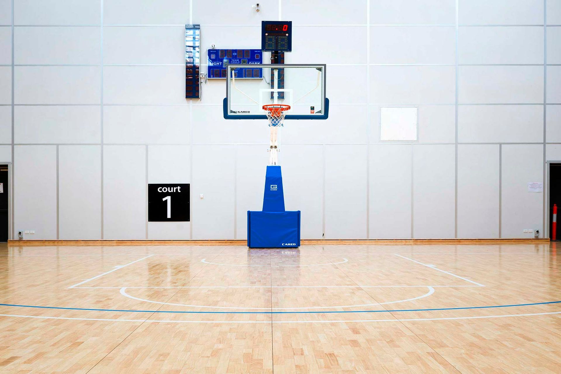 An empty basketball court with a basketball hoop and a scoreboard.