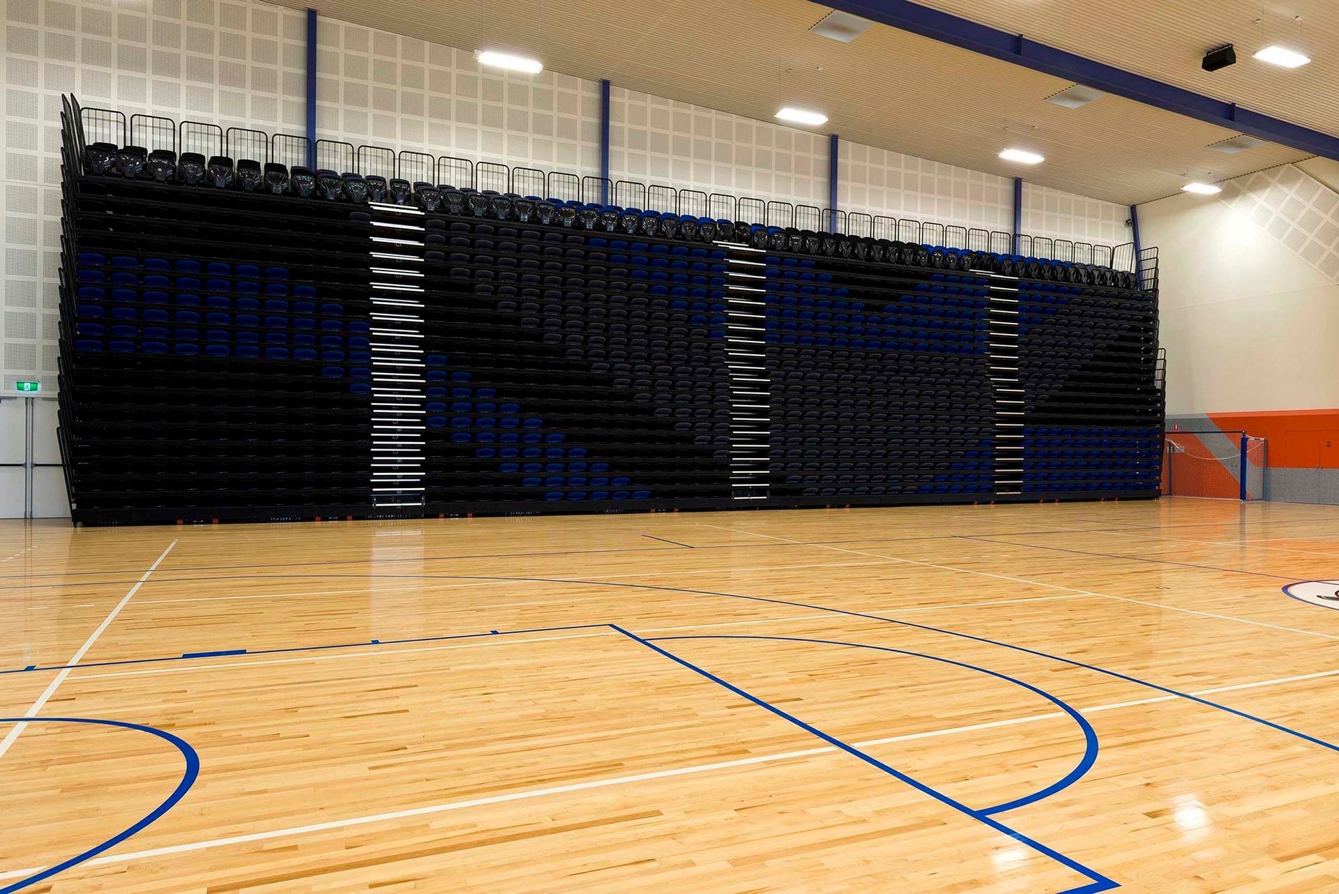 A basketball court with a wooden floor and bleachers in the background.