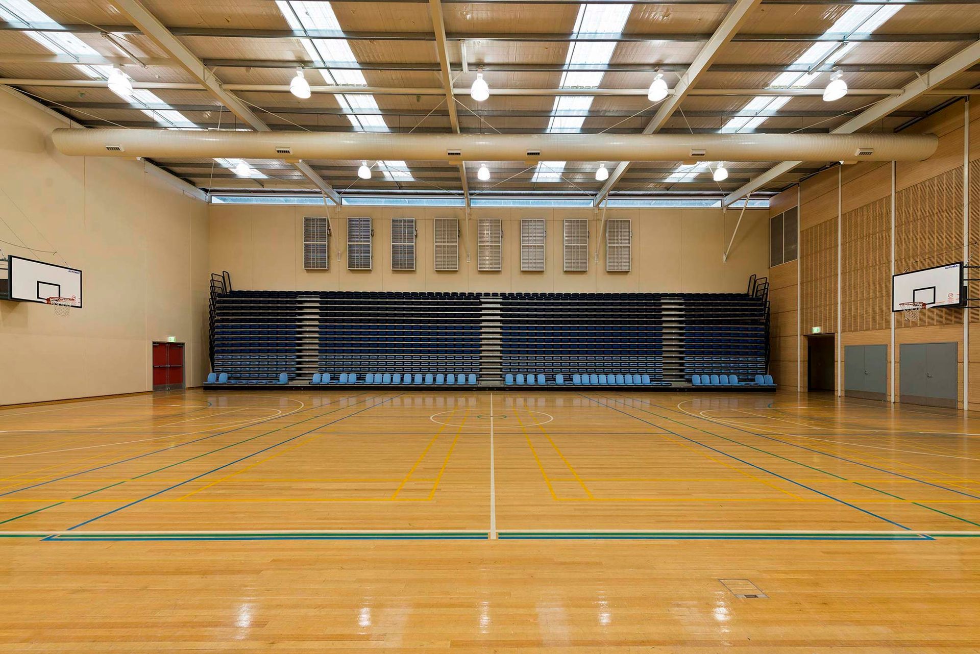 An empty basketball court in a gym with bleachers and a basketball hoop.