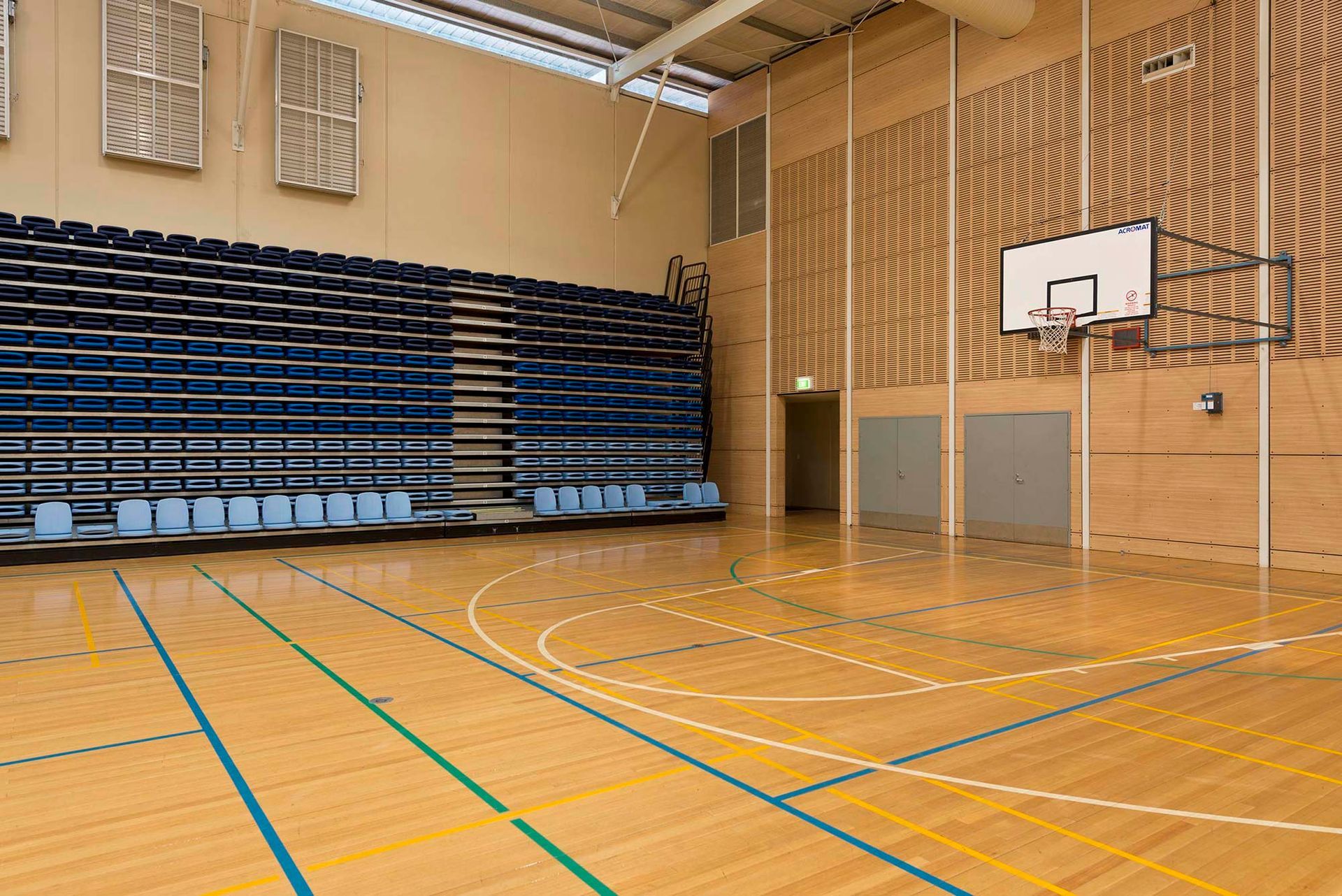 An empty basketball court with bleachers and a basketball hoop.