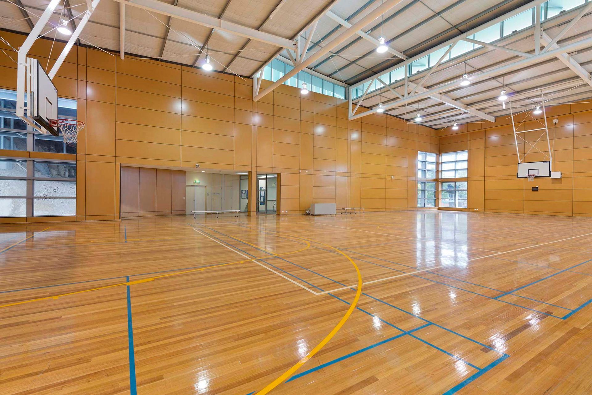 An empty basketball court with a wooden floor and a basketball hoop.