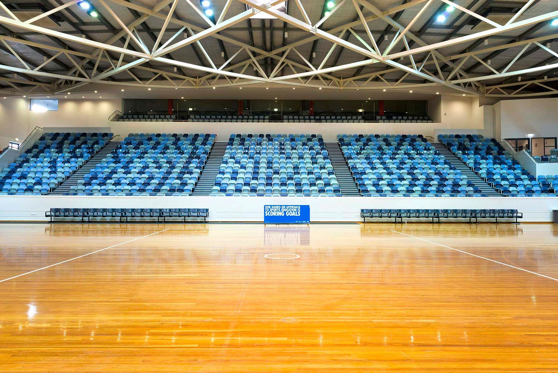 An empty basketball court with bleachers and a basketball hoop.