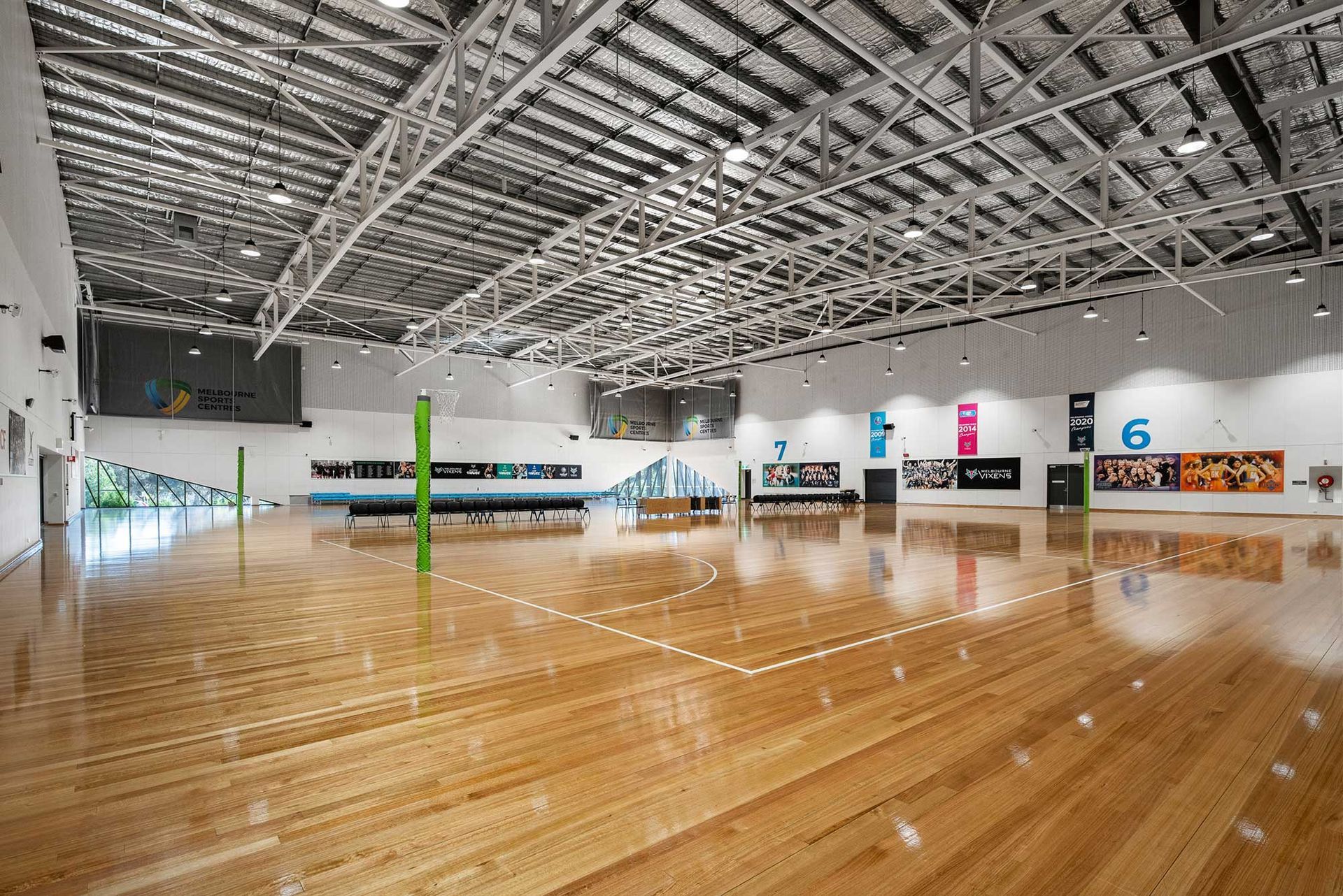 A large empty gym with a wooden floor and a green pole in the middle.