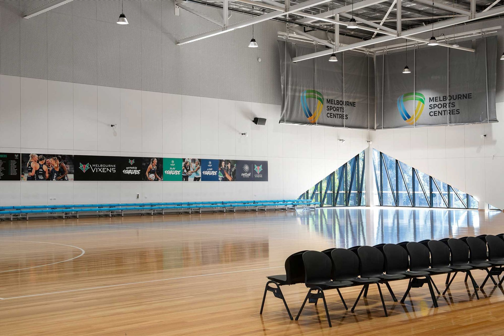 A row of chairs are lined up in front of an empty basketball court.