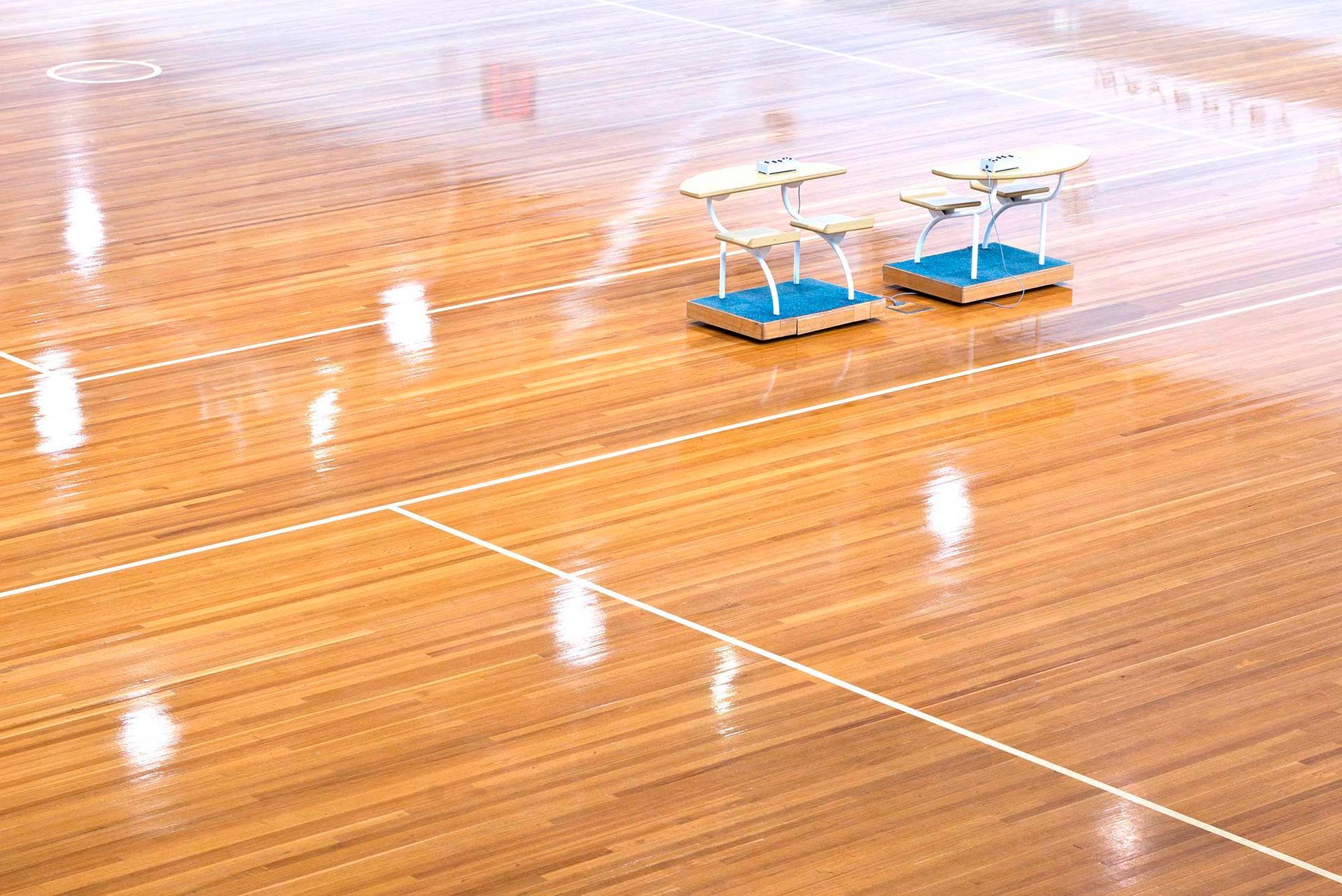 A wooden floor in a basketball court with two tables on it.
