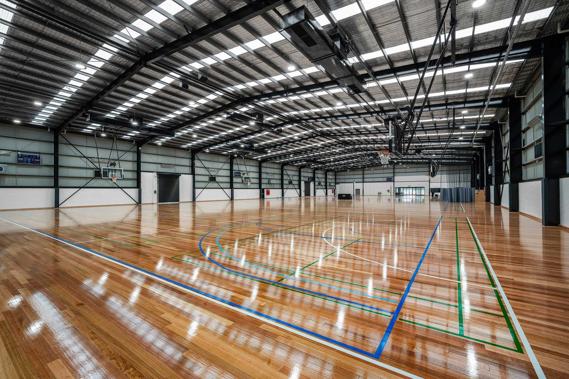 A large empty gym with a wooden floor and a basketball hoop.