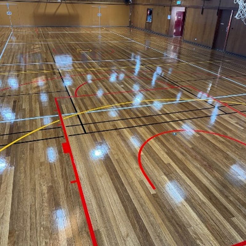 Indoor basketball court with newly polished timber surface, showcasing high-quality commercial flooring services. Indoor basketball court with newly polished timber surface, showcasing high-quality commercial flooring services.