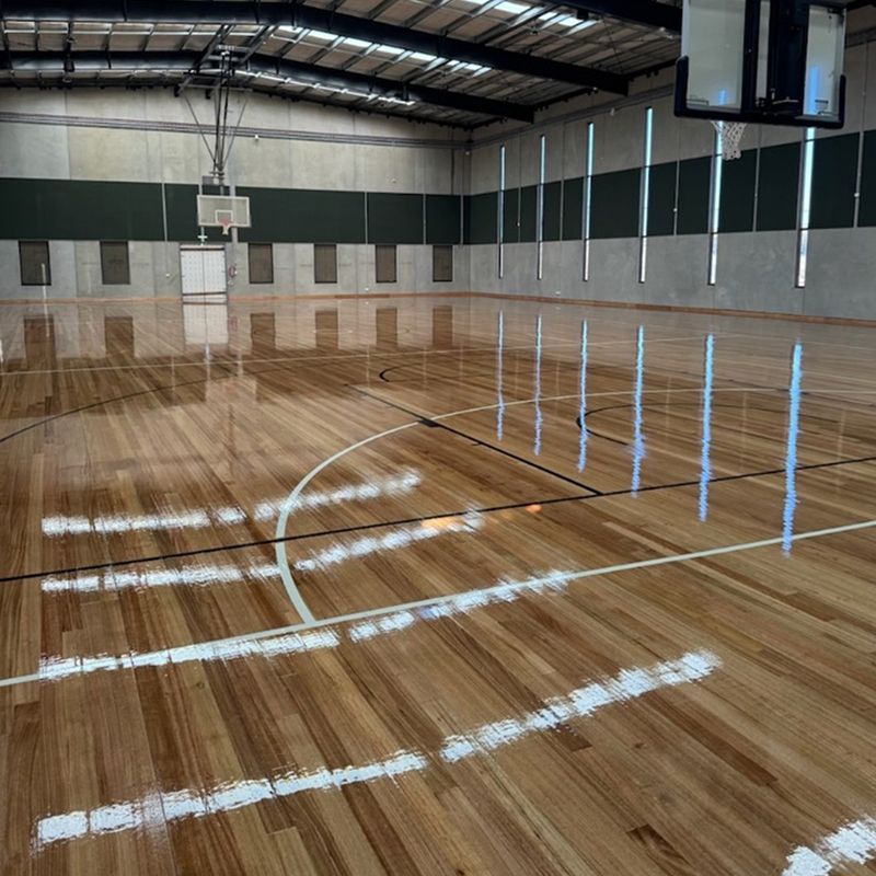 Modern sports facility featuring freshly finished timber basketball court, highlighting expert commercial flooring services Modern sports facility featuring freshly finished timber basketball court, highlighting expert commercial flooring services