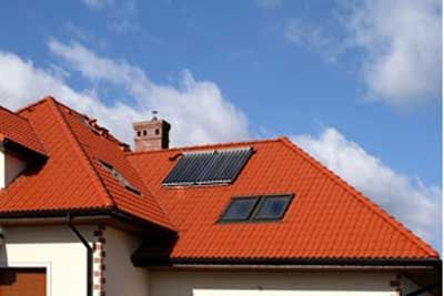 Tetto di tegole rosse con pannelli solari e camino sotto un cielo azzurro