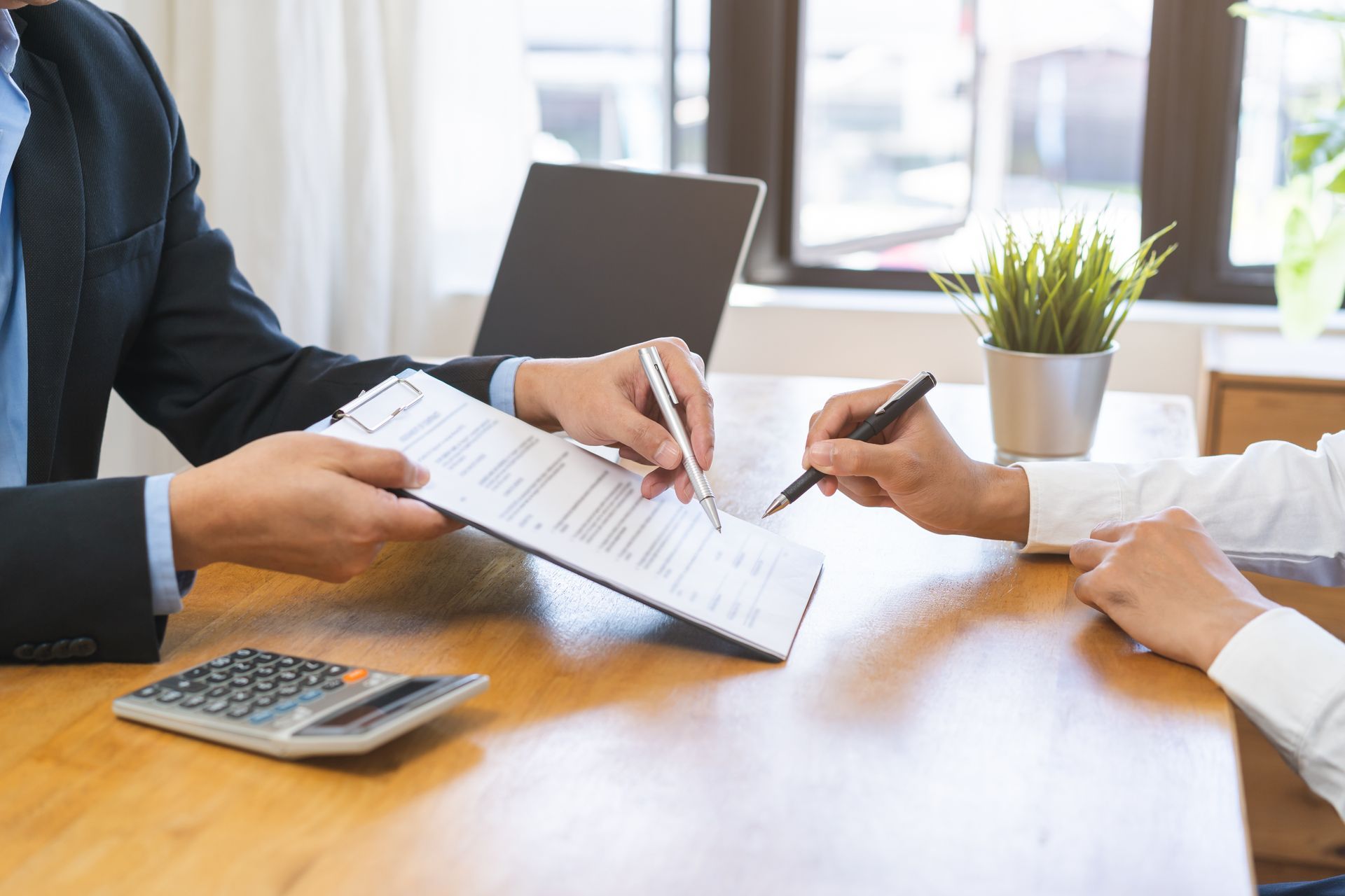 Two people at a desk signing a document. A suit jacket points to where to sign.
