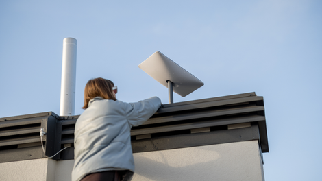 Person installing a satellite dish on a rooftop; clear blue sky.