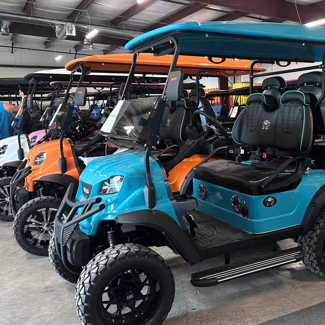 A row of golf carts are parked in a warehouse.