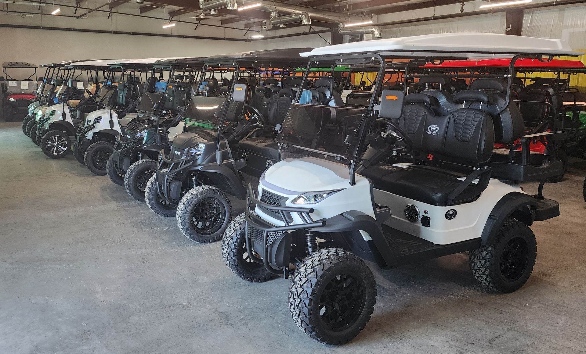 A row of golf carts are lined up in a warehouse.