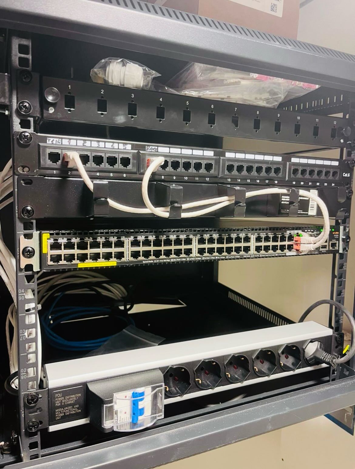 Rack per server nero con hardware di rete: pannelli di permutazione, switch e una ciabatta.