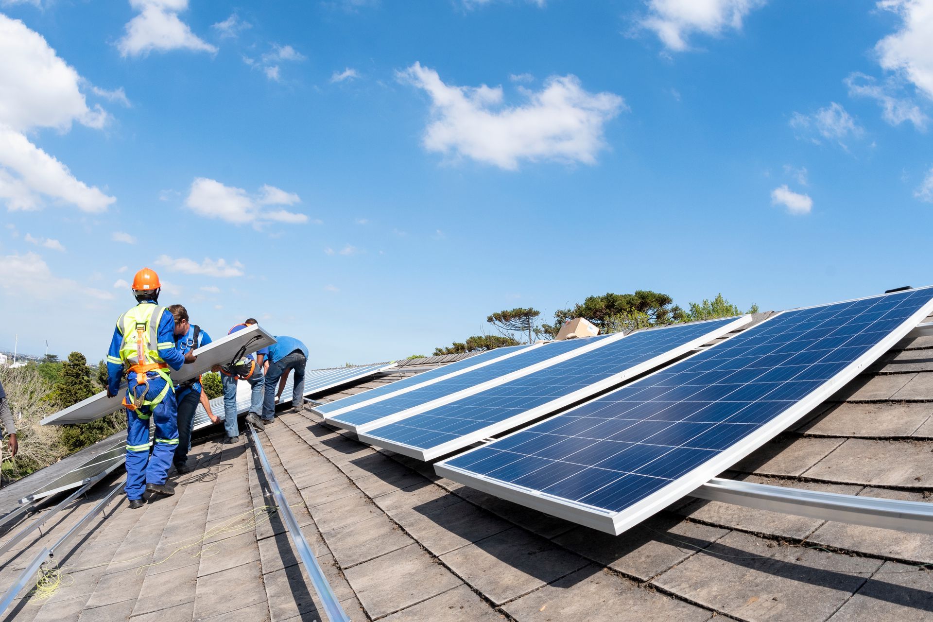 Operai che installano pannelli solari su un tetto contro un cielo azzurro con nuvole.