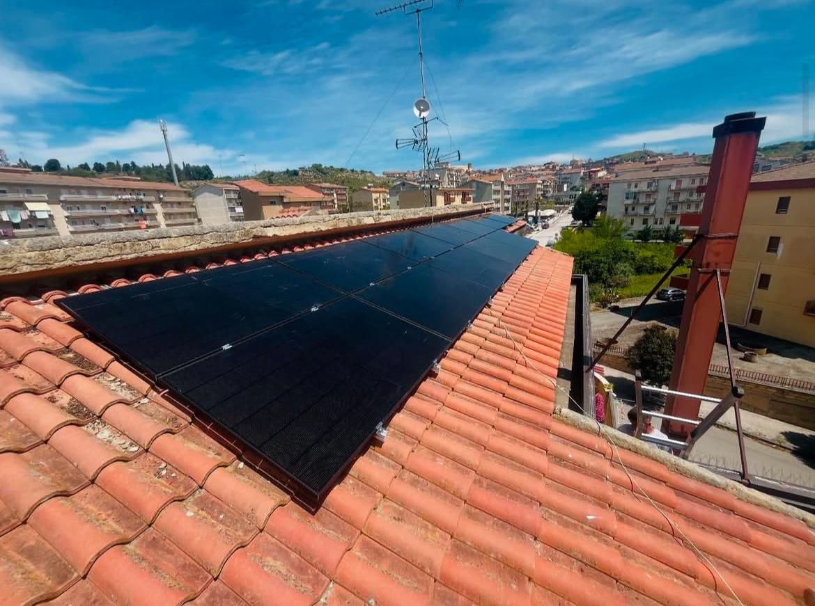 Pannelli solari installati su un tetto di tegole, con un paesaggio suburbano sullo sfondo.