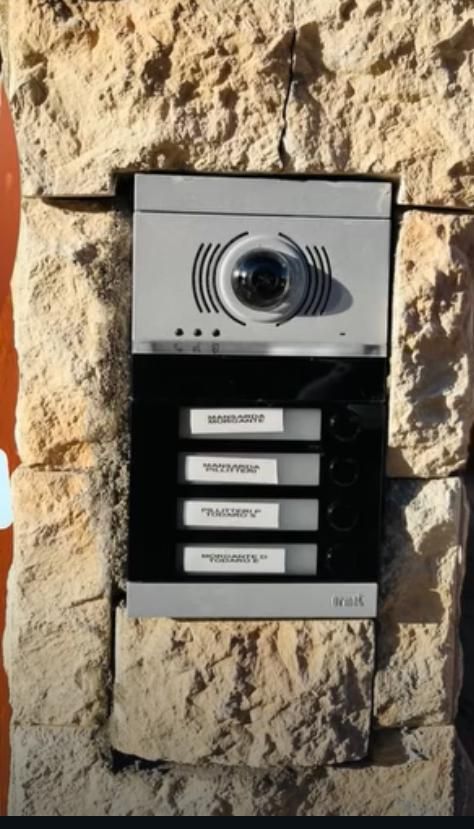 Tastiera di sicurezza e sistema di interfono montati su una parete bianca.