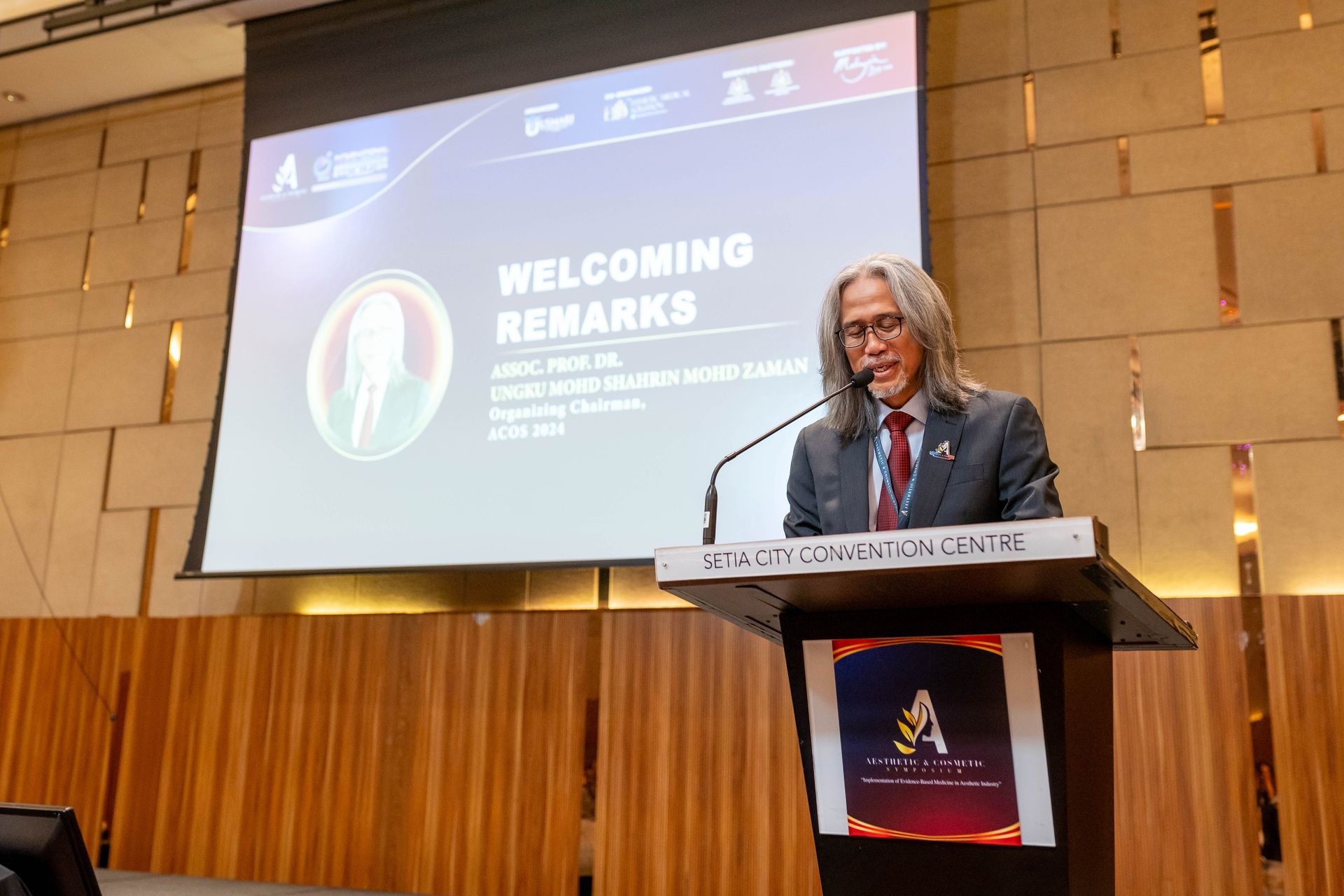 Man with long hair speaks at a podium;