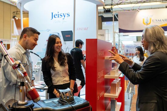 People at a trade show booth, looking at display and equipment; man explaining details, a red display.
