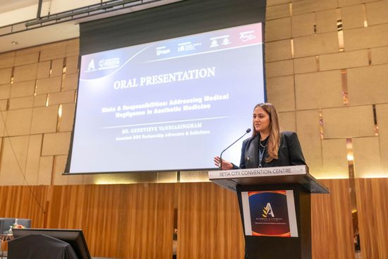 Woman giving an oral presentation at a conference, standing at a podium. Presentation title on screen: 