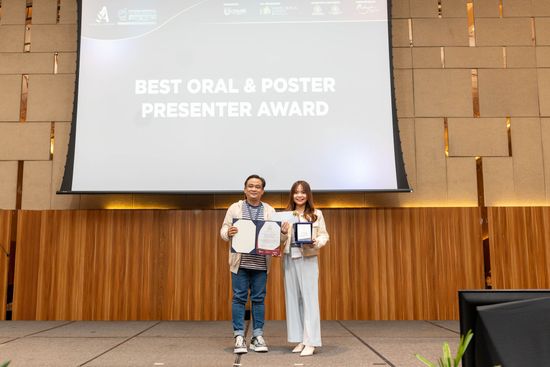 Two people holding awards on a stage with a screen that reads 