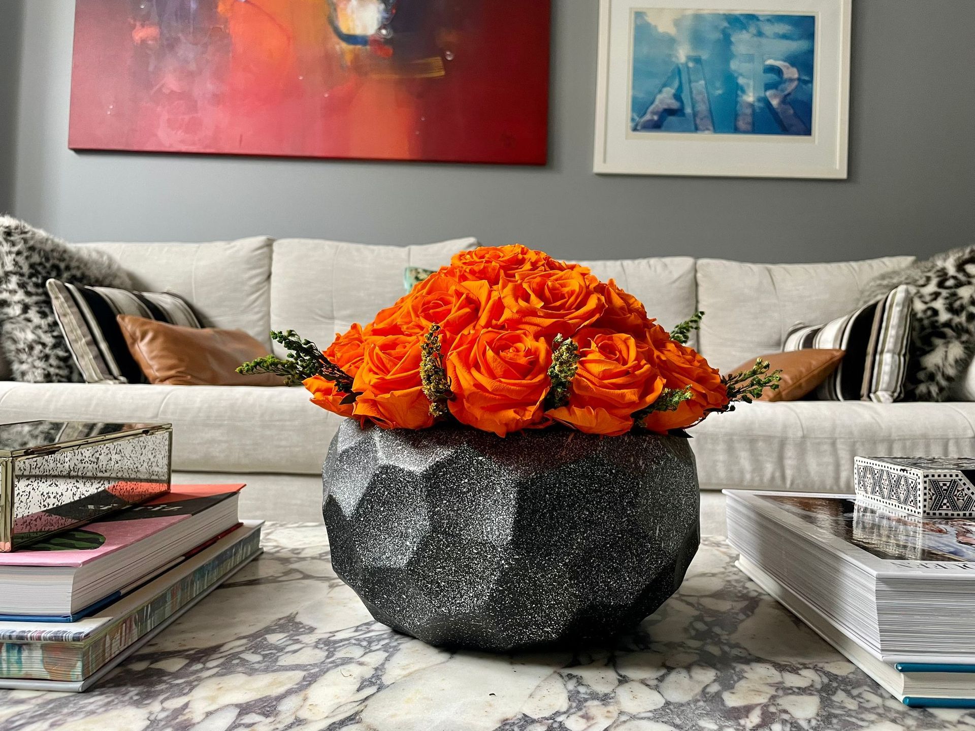 Bespoke orange rose centerpiece in a black textured vase on a marble table.