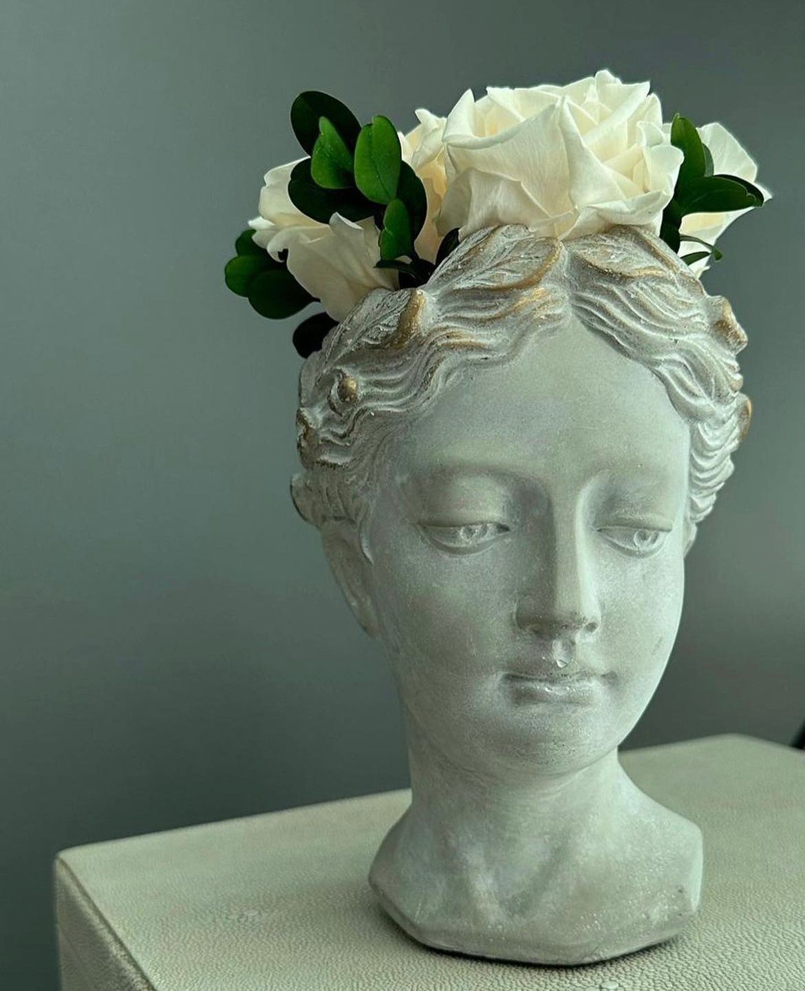 Stone bust of a woman with white roses and green leaves.