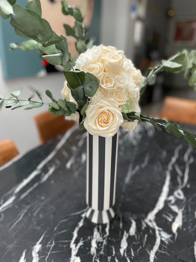 A bespoke arrangement with  black and white striped vase holding white roses and eucalyptus 