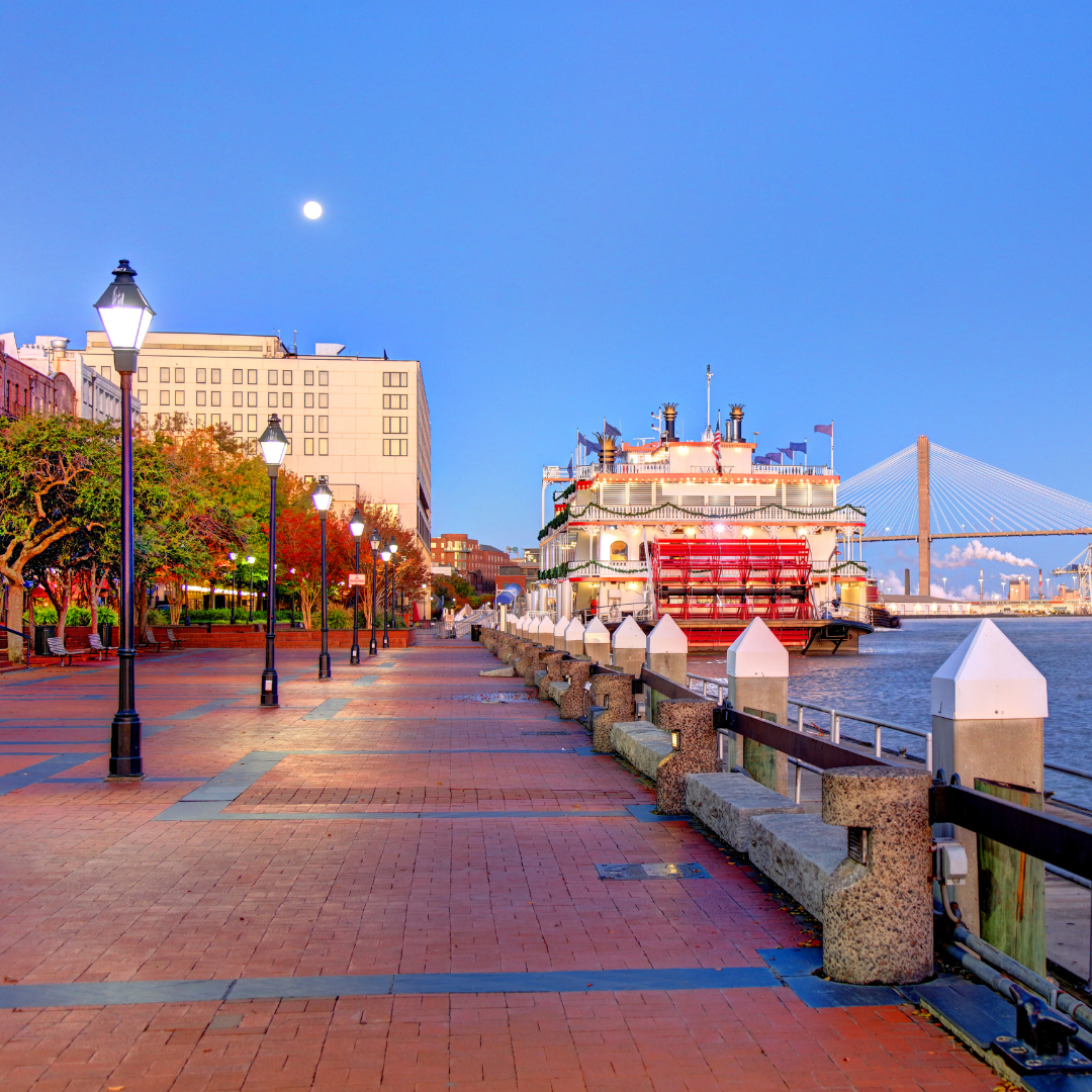 A boat is docked at a dock with a bridge in the background in Savannah Georgia.