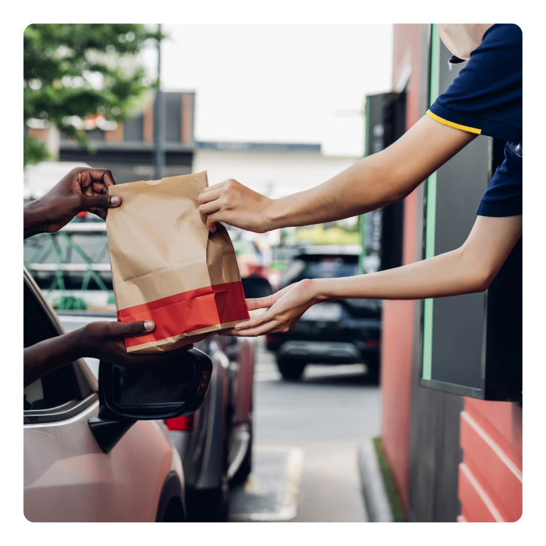 A person is handing a bag of food to another person from a fast food window. 