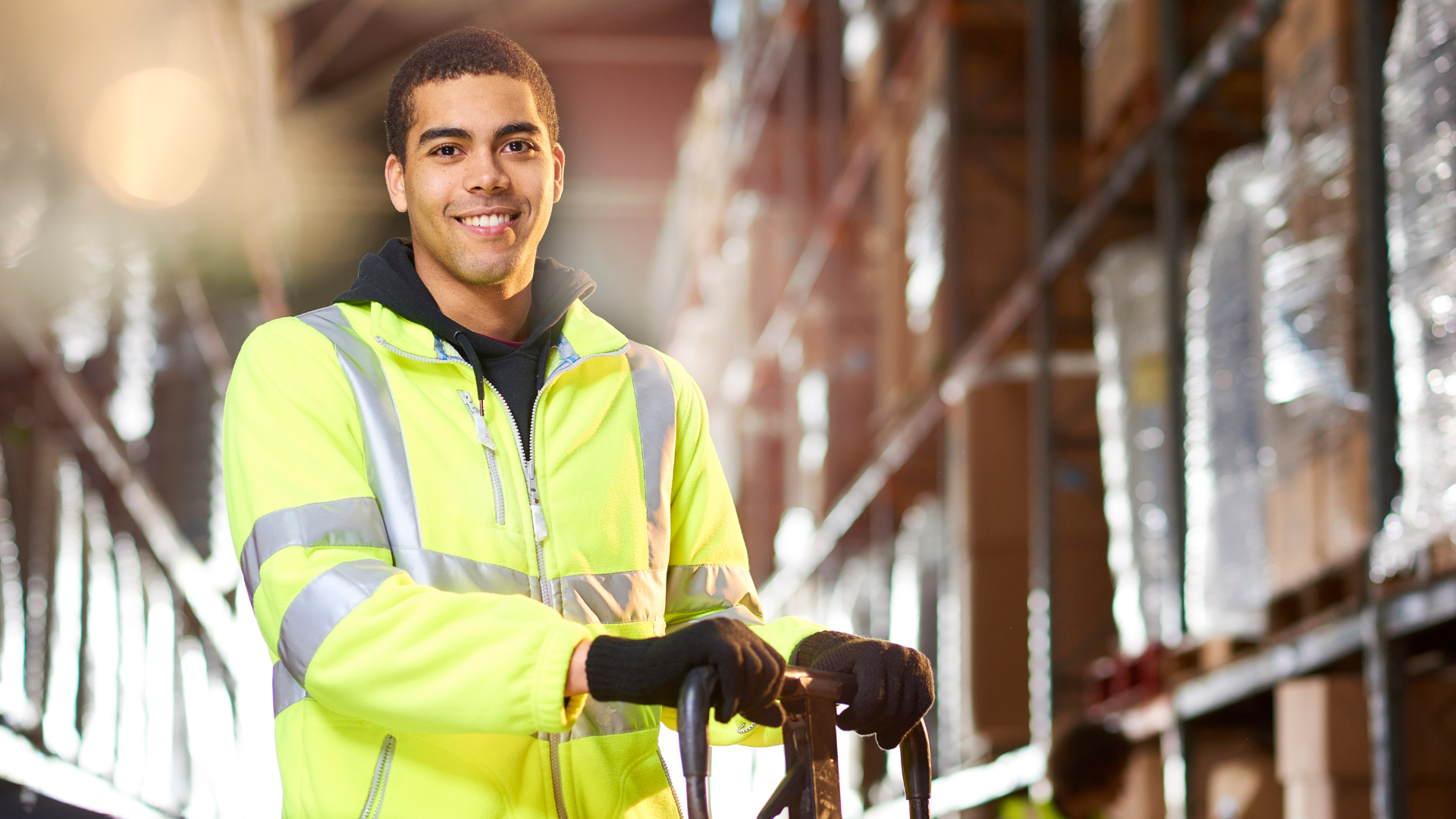 A man in a yellow jacket is pushing a cart in a warehouse.