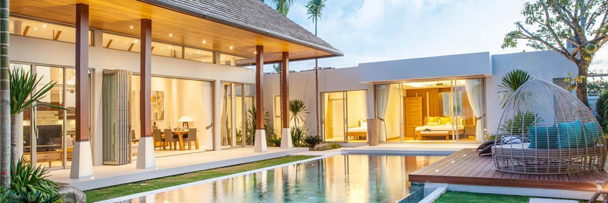 A luxurious villa with a pool. The home features open glass doors, wooden pillars, and a serene water view.