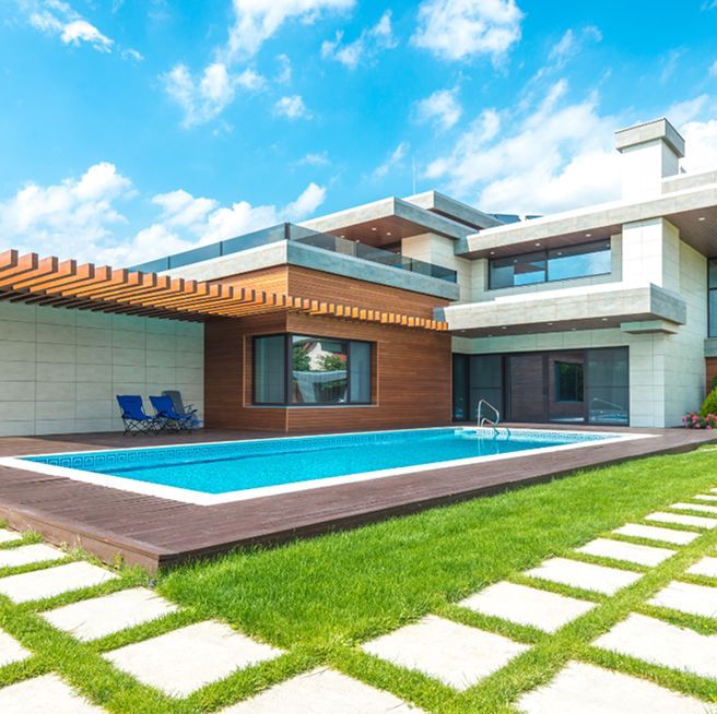 Modern house with a pool and lush lawn under a bright blue sky.