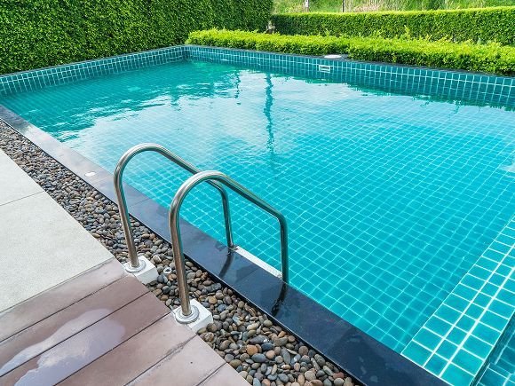 Swimming pool surrounded by green foliage under a blue sky.