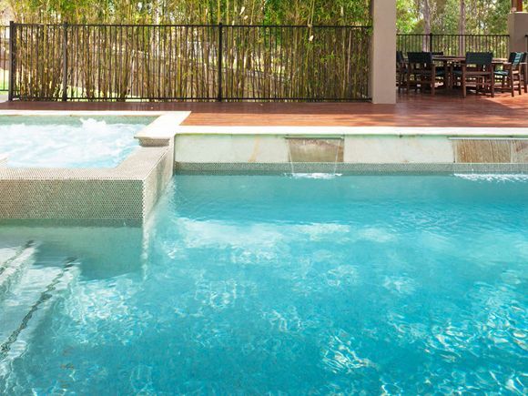 Swimming pool surrounded by green foliage under a blue sky.