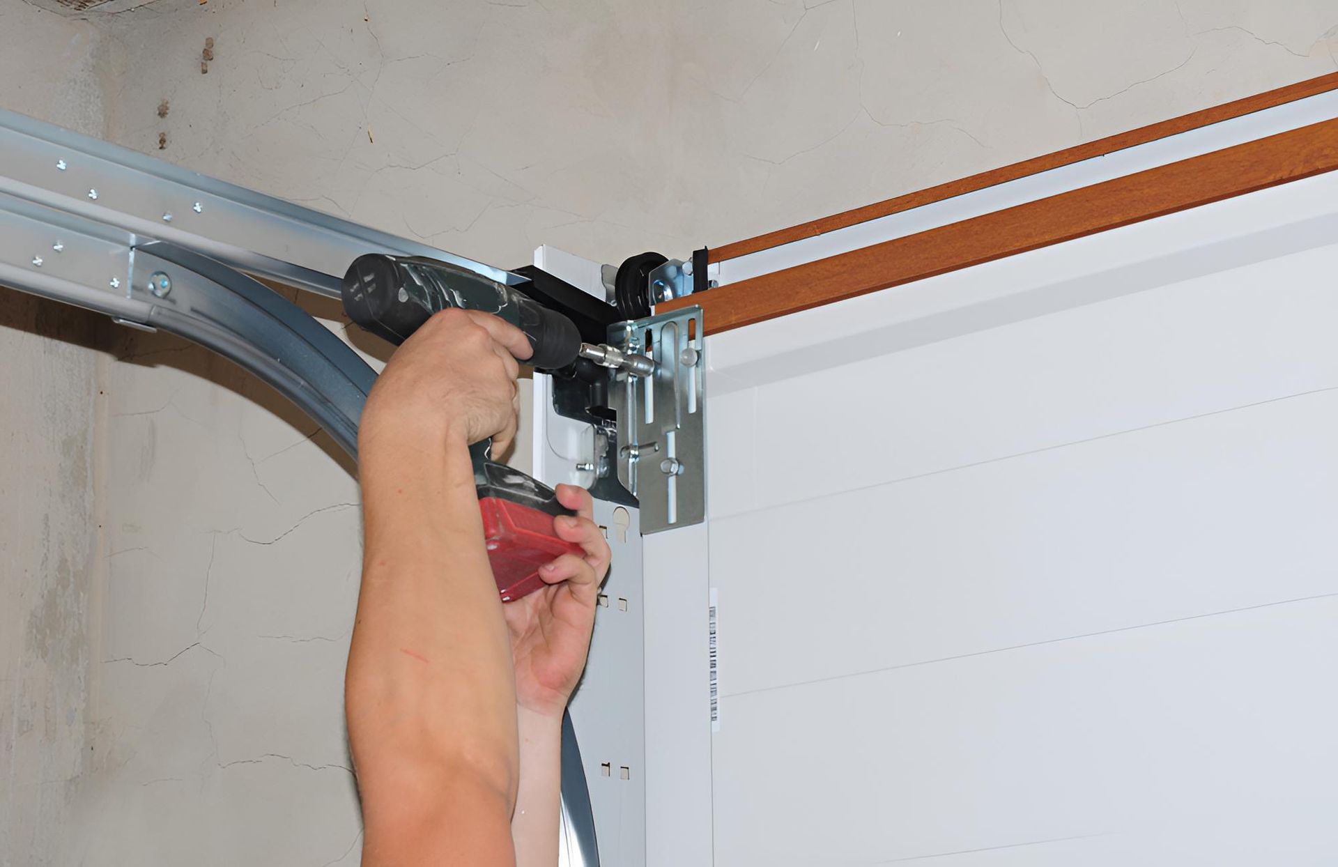 Person using a power drill to install garage door hardware near the ceiling. — Automated Garage Doors in Deebing Heights, QLD