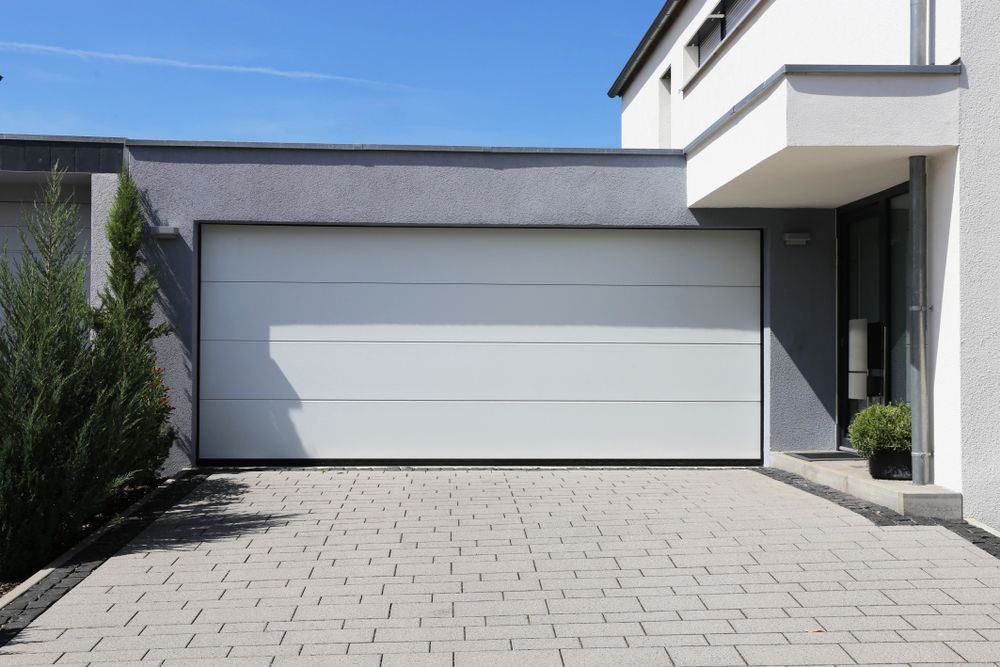 White garage door on a modern house with a gray driveway and blue sky. — Automated Garage Doors in Ripley, QLD