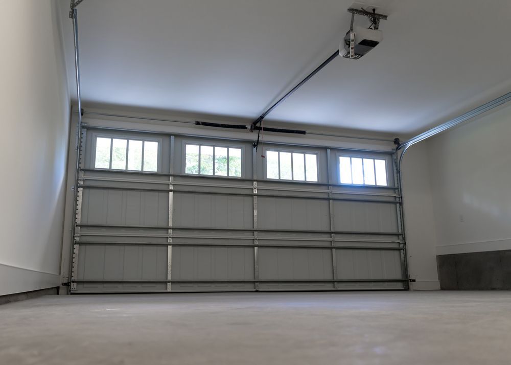 Interior of an empty garage with a partially open, white garage door and windows. — Automated Garage Doors in Redbank Plains, QLD