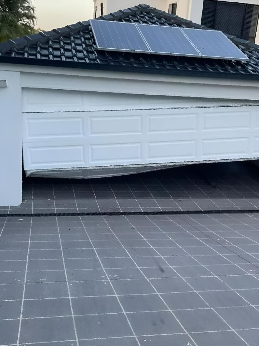 A White Garage Door is Visibly Damaged and Sagging Open — Automated Garage Doors in Chuwar, QLD