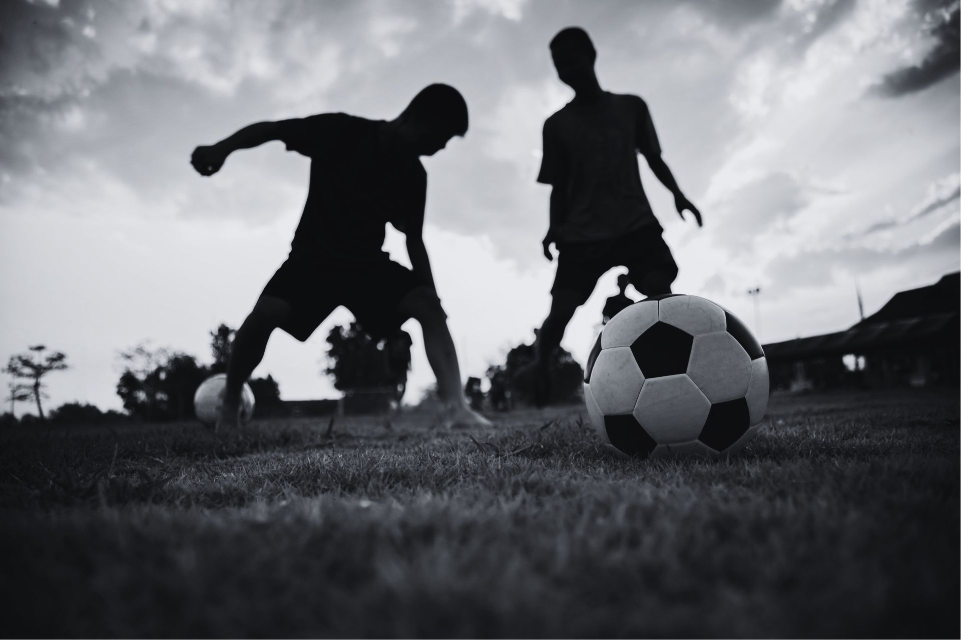 Two boys silhouetted playing soccer on a grassy field at sunset.