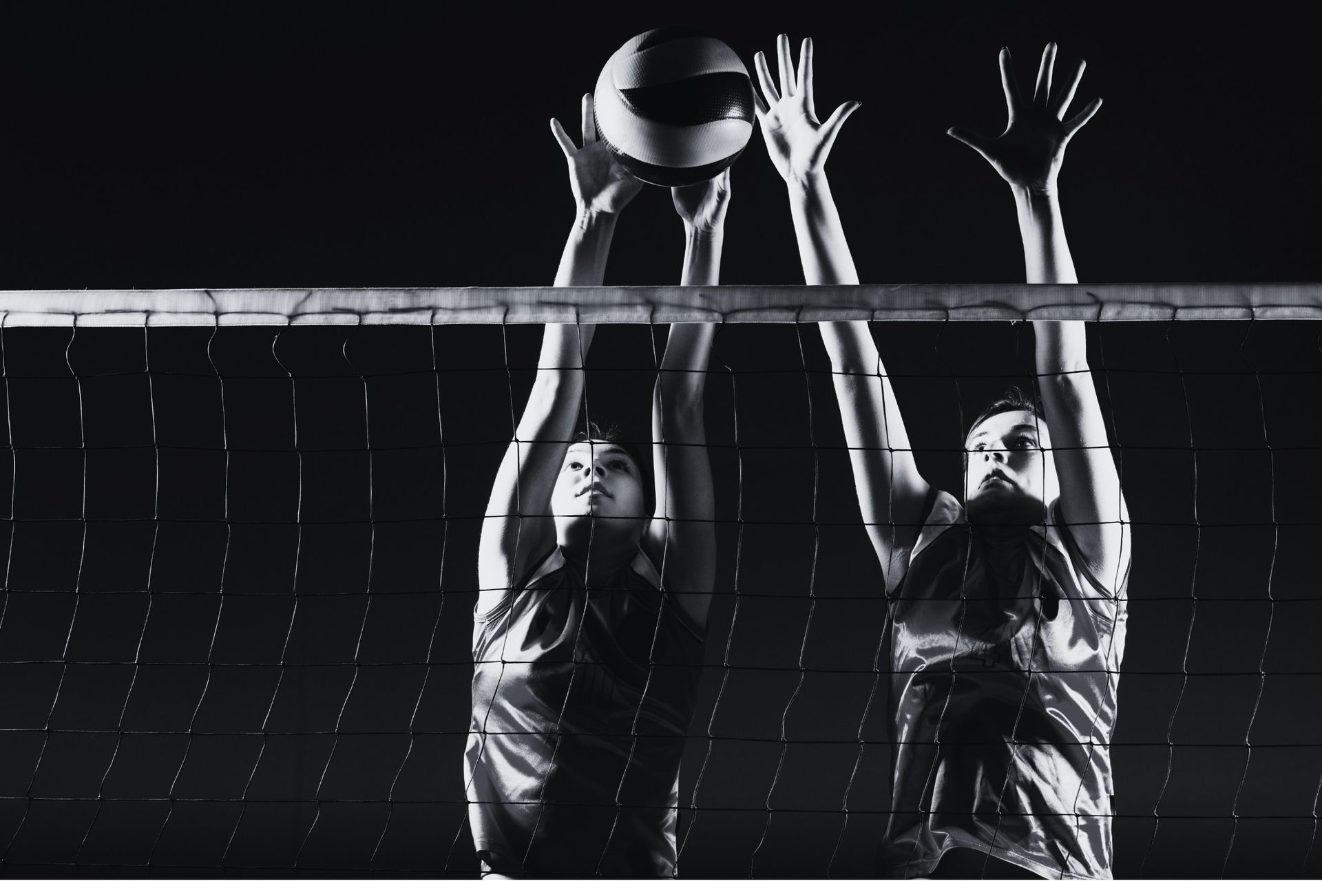 Two volleyball players jumping to block the ball at the net.