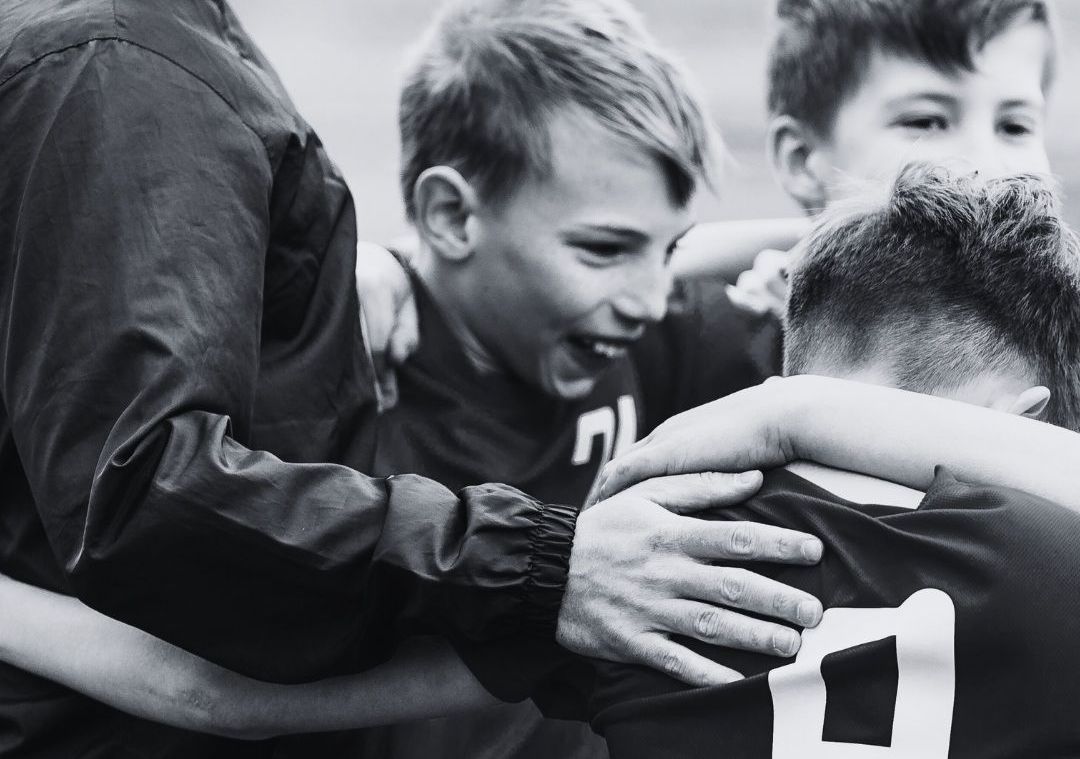 A group of young boys are hugging each other in a black and white photo.