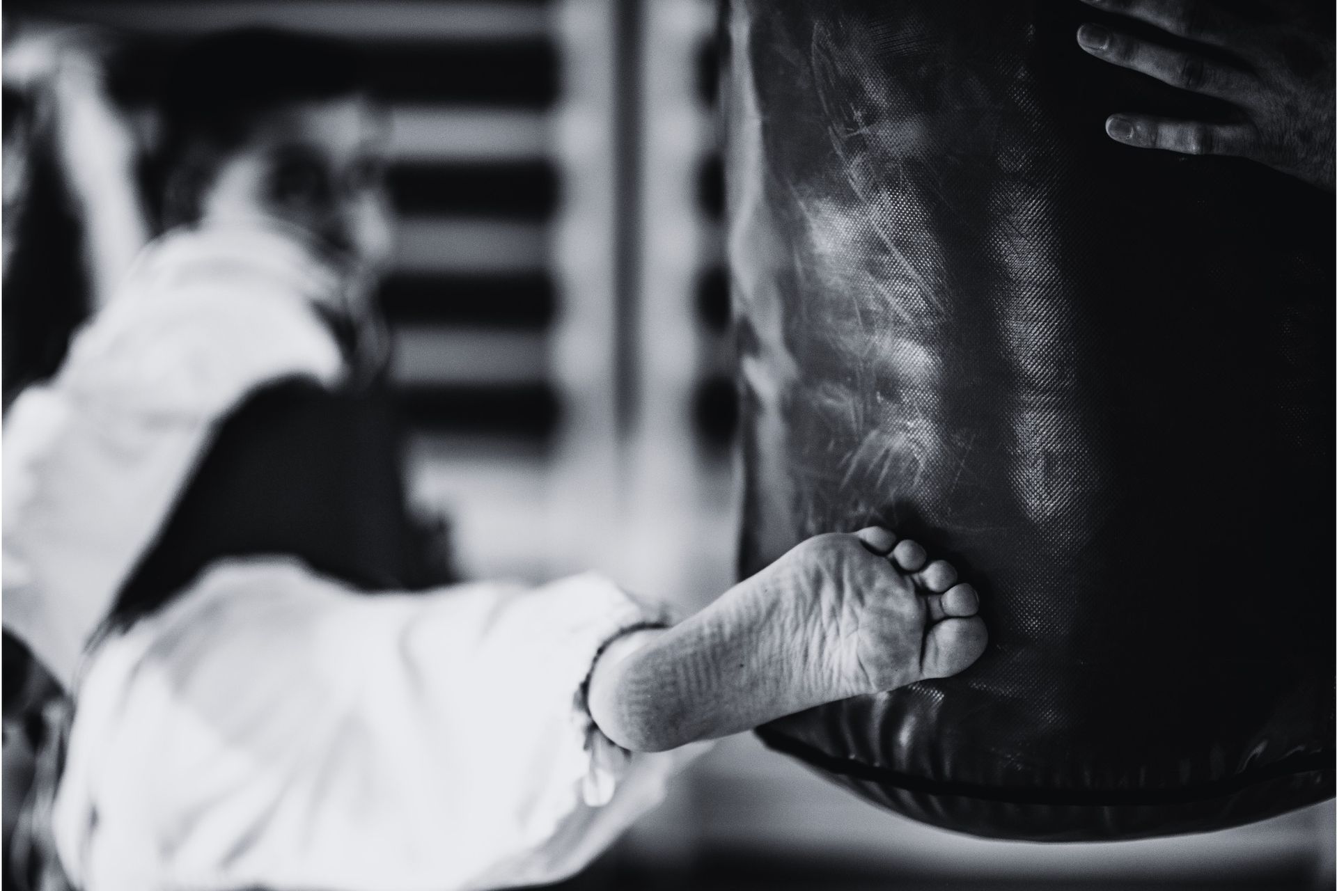 A person in a karate uniform kicks a heavy bag. Black and white photo.