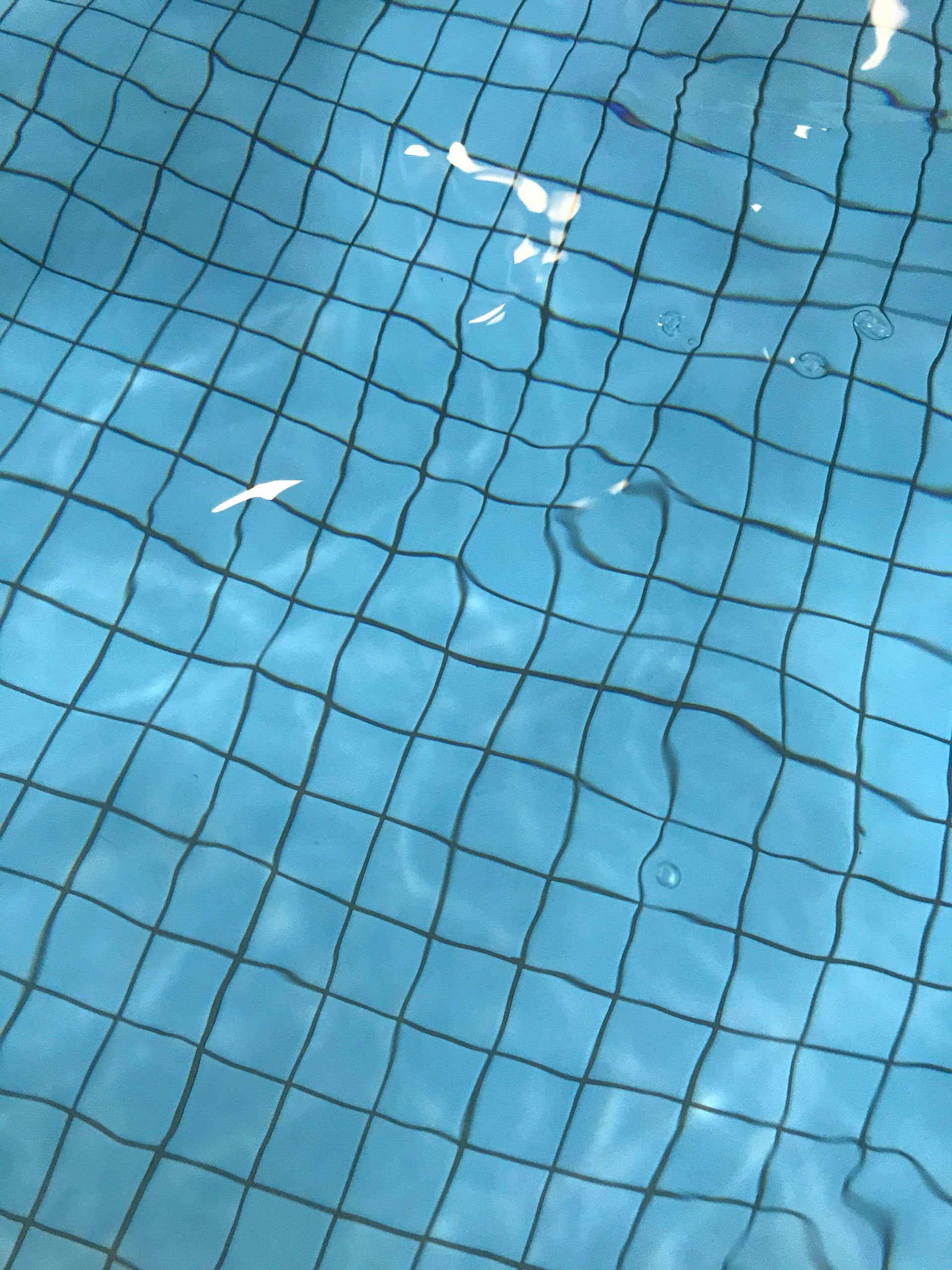 Blue water in a pool, rippled with a black grid pattern visible underneath.